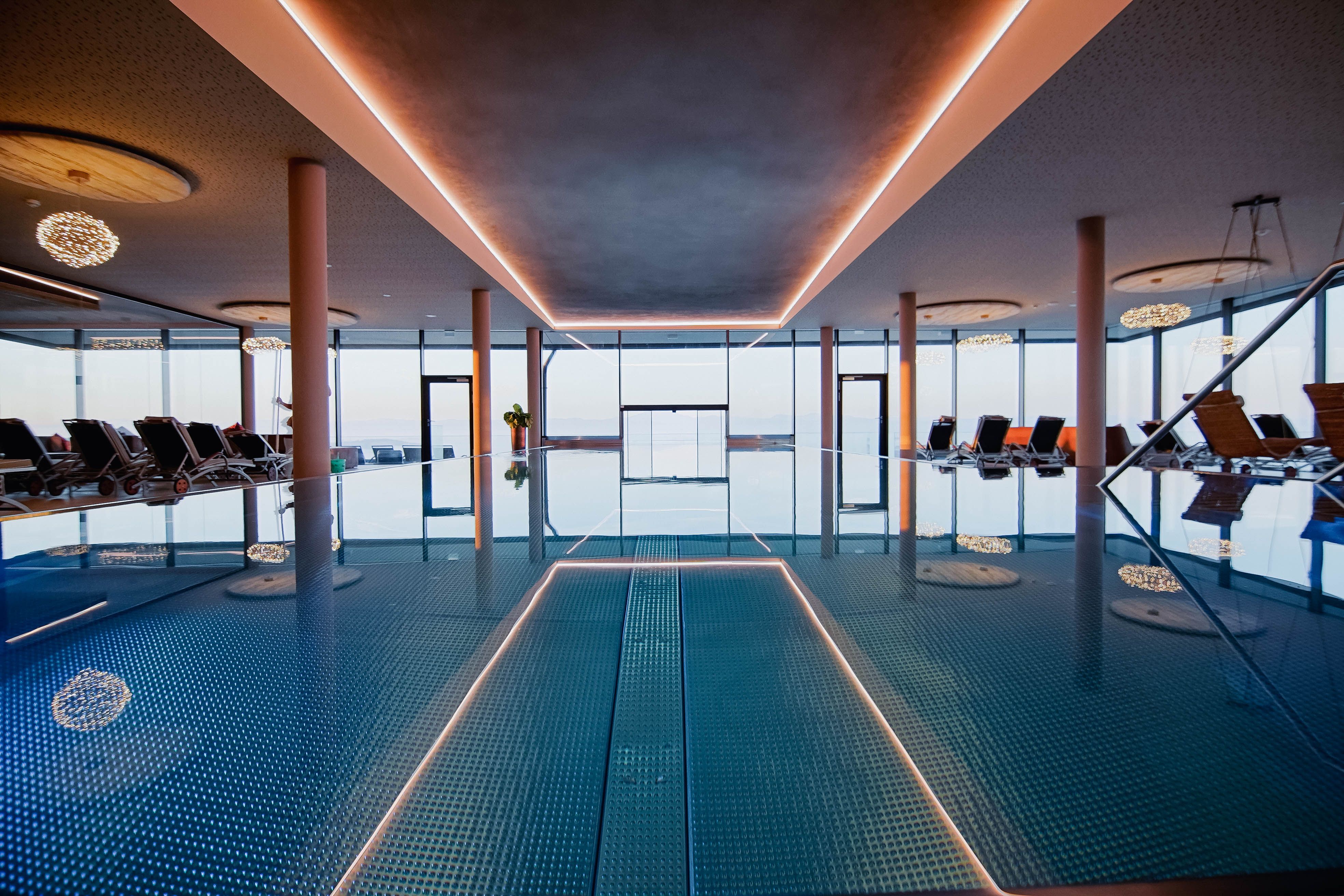 Interior view of an infinity pool with sun loungers and large windows.