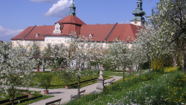 Historic courtyard garden with blossoming trees and a large building in the background.