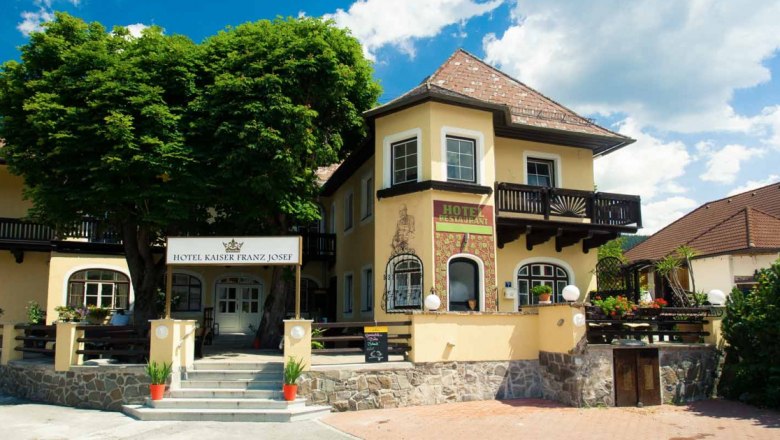Entrance to the Hotel Kaiser Franz Josef with yellow fa&ccedil;ade and balcony.