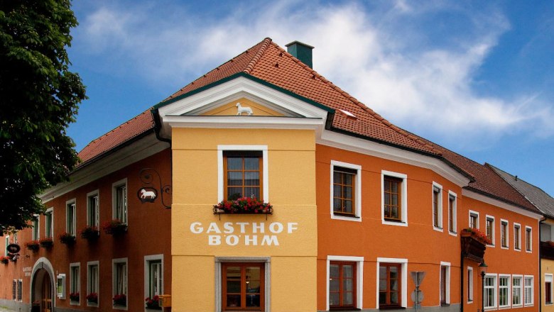 A traditional inn with an orange and yellow façade and red roof tiles under a blue sky.