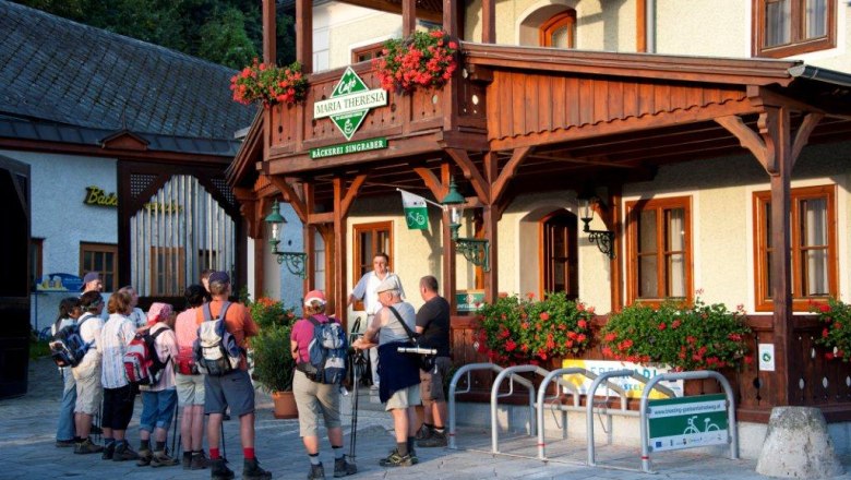 A group of hikers stands in front of the Caf&eacute; Maria Theresia with its wooden veranda and floral decorations.