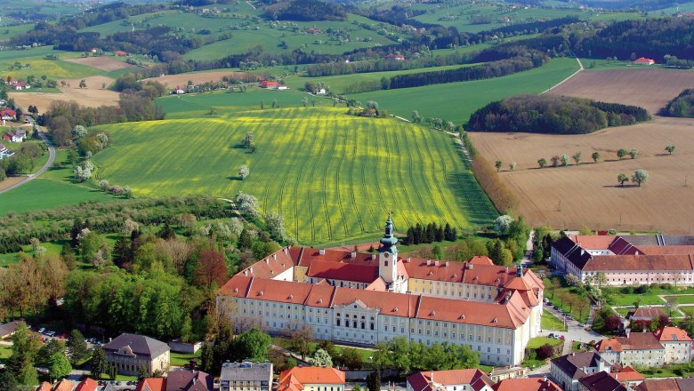 Aerial view of Seitenstetten Benedictine Abbey surrounded by green fields and hills.