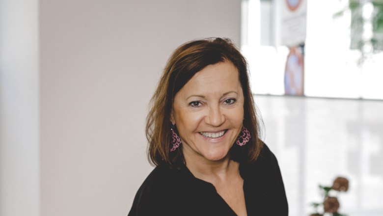 A woman in black clothing serves a dish of tomatoes and fish in a restaurant.