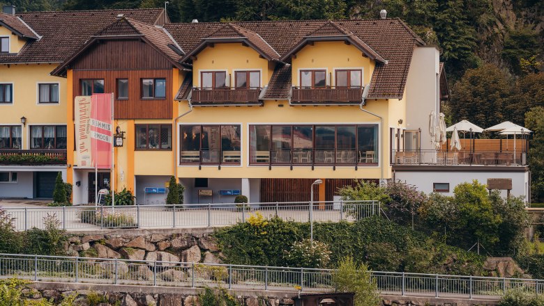 Yellow building with terrace and signs, surrounded by trees.