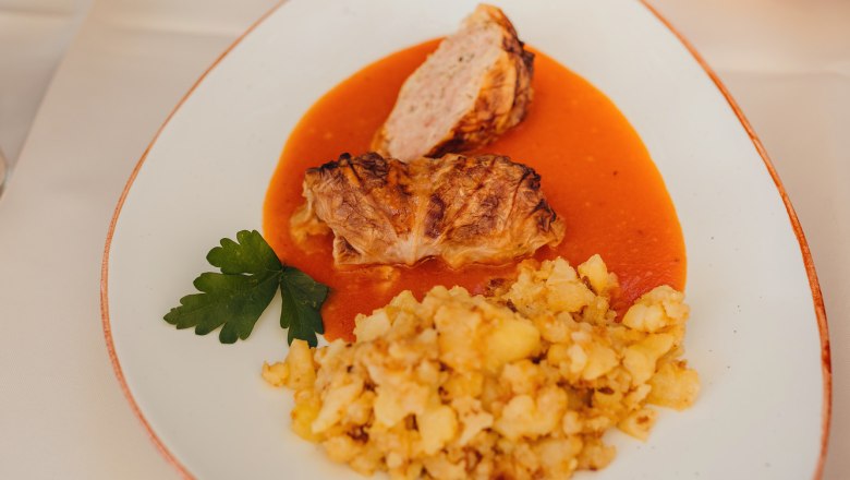 Cabbage roulade with potatoes and gravy served on a white plate.