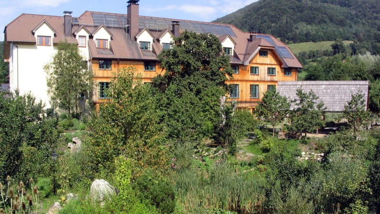 A large building with a wooden façade, surrounded by lush greenery and a mountain in the background.