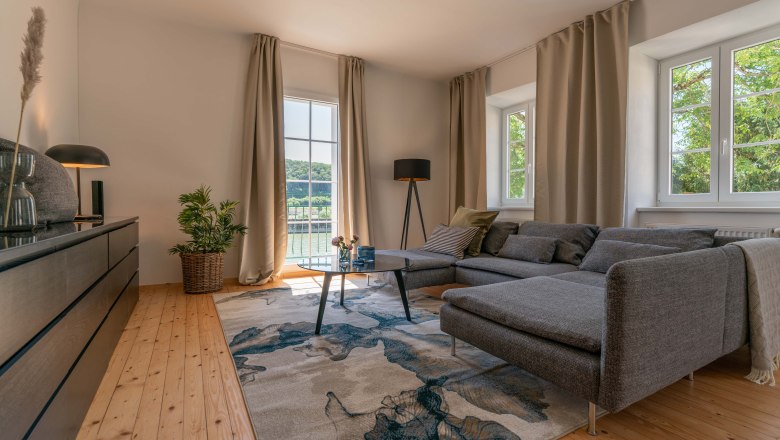 Modern living room with gray sofa, wooden floor and large window with a view of the greenery.