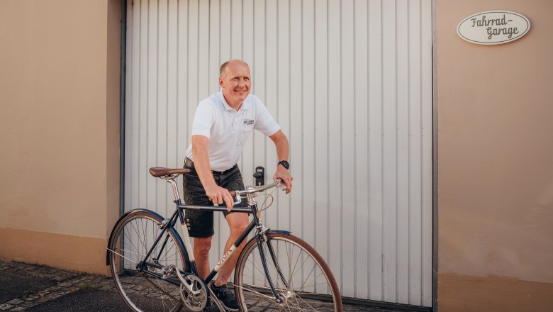 Man in white polo shirt riding bicycle in front of garage door.