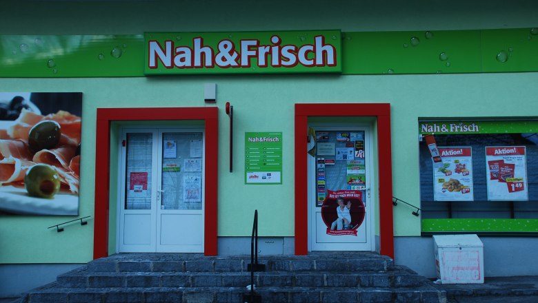 Entrance of a Nah&Frisch store with advertising posters and shop window.
