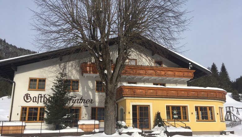 An inn in the snow with wooden decorations and a large tree in front of it.