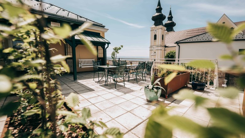 Terrace with table and chairs, church tower with two spires in the background.