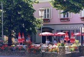 Exterior view of an inn with terrace, red parasols and floral decorations.
