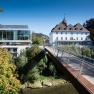 Modern and historic building with bridge in green surroundings.