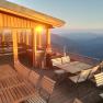 Terrace with wooden furniture and mountain views at sunset.