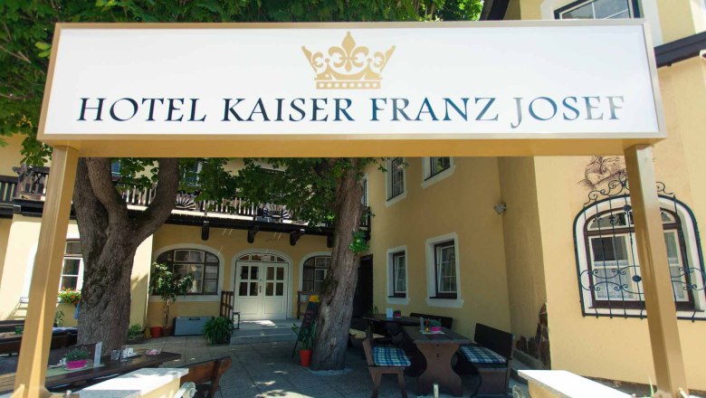 Entrance to the Hotel Kaiser Franz Josef with sign and trees.