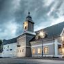 A hotel with a bell tower under a cloudy sky, illuminated by streetlights.