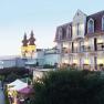 A hotel with balconies and a church in the background at dusk.