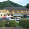 Yellow guesthouse with balcony and parasols in front of a wooded hill.