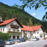 A traditional inn with red roofs and flower boxes, surrounded by woods and parked cars.