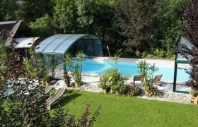 A covered outdoor pool with sun loungers and plants, surrounded by greenery.