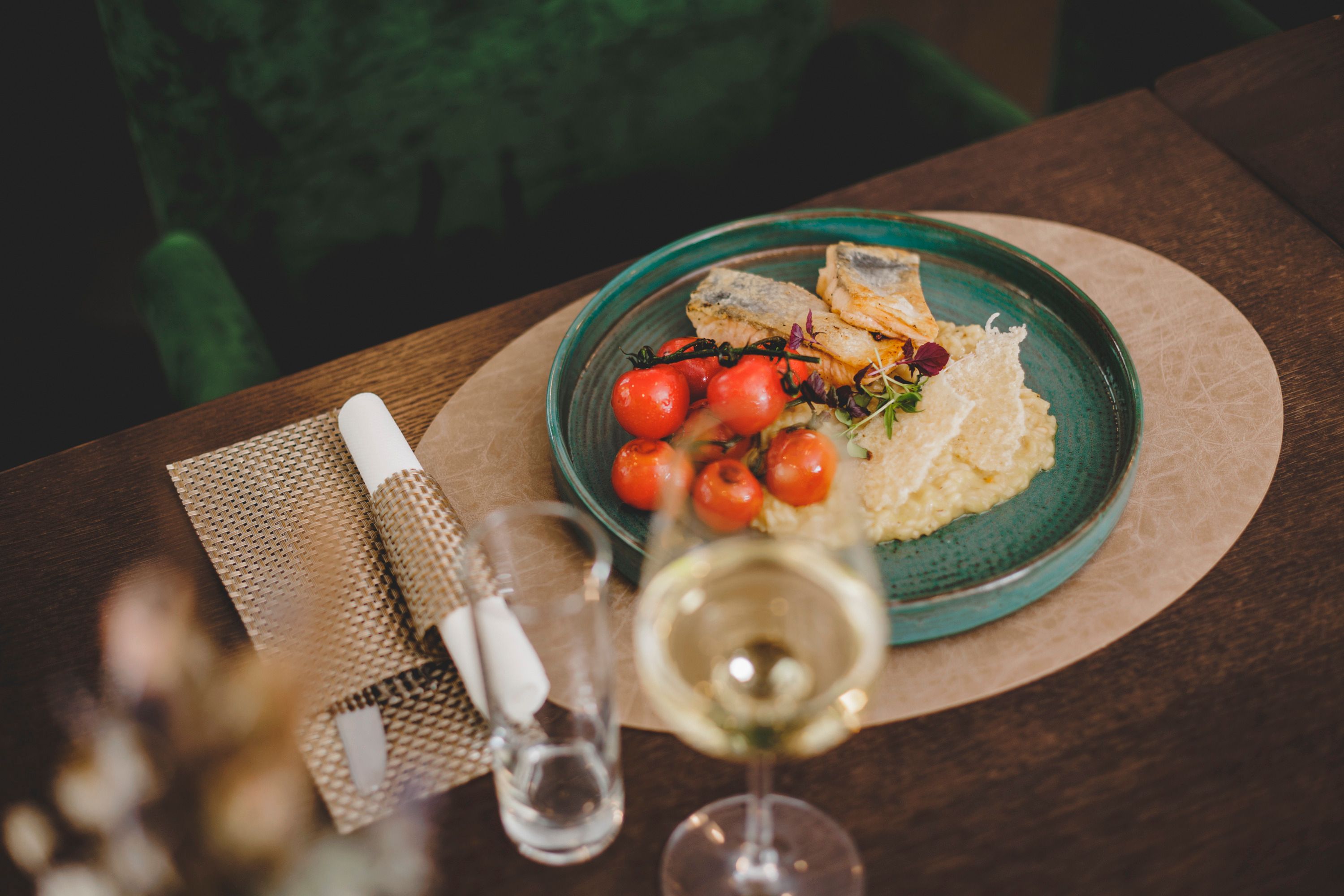 A plate of grilled gilthead bream fillet, lemon risotto and cherry tomatoes, served on a wooden table with a glass of white wine.