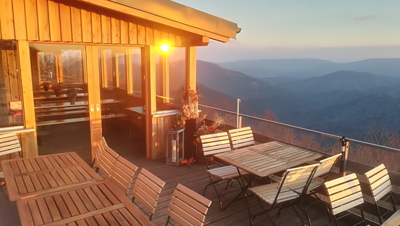 Terrace with wooden furniture and mountain views at sunset.