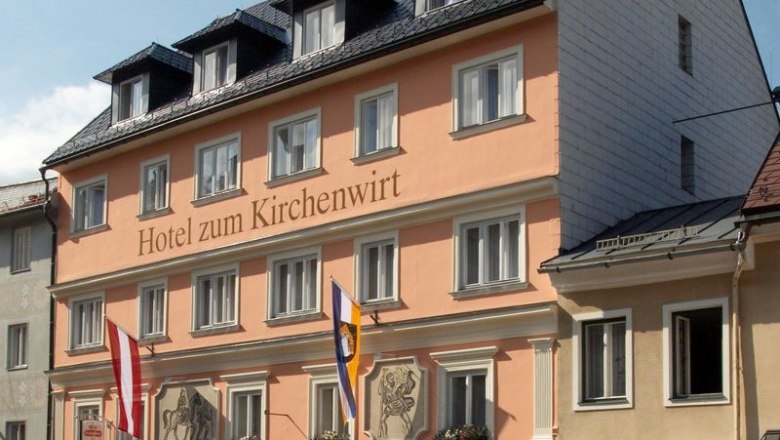 Facade of the Hotel zum Kirchenwirt with flags and blue sky.