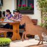 Two women sit at a wooden table outdoors and eat. In the foreground is a metal sculpture of a horse.