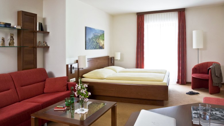 Cozy hotel room with double bed, red sofa, glass table and decorations.
