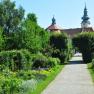 A well-kept garden path with flowers and trees, in the background a historic building with towers.