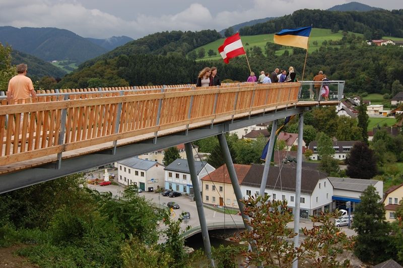 People on a wooden platform with Austrian and Ukrainian flags, a rural landscape in the background.