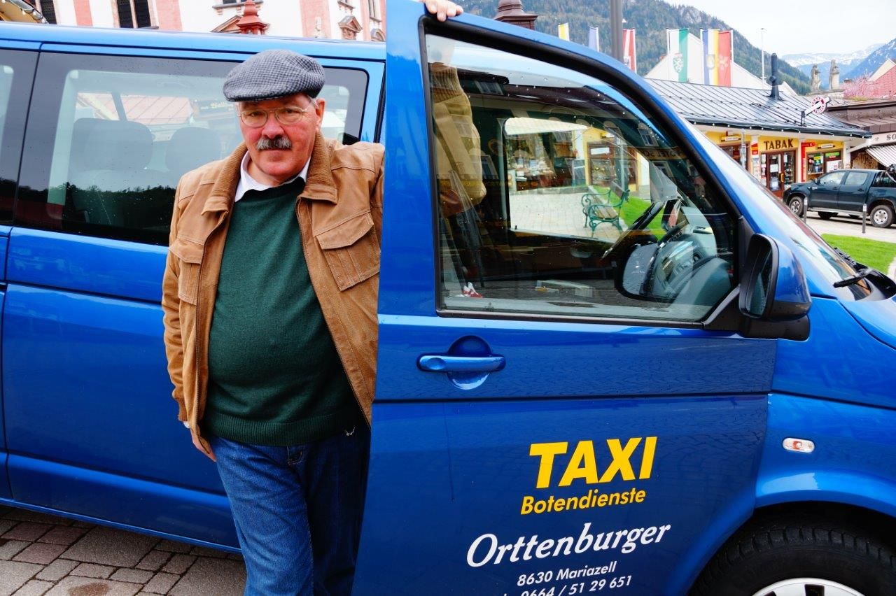 A man is standing next to a blue cab with the sign 'Taxi Botendienste Orttenburger'.