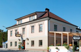 A traditional inn with a pink fa&ccedil;ade and red roof, decorated with plants and a pumpkin.