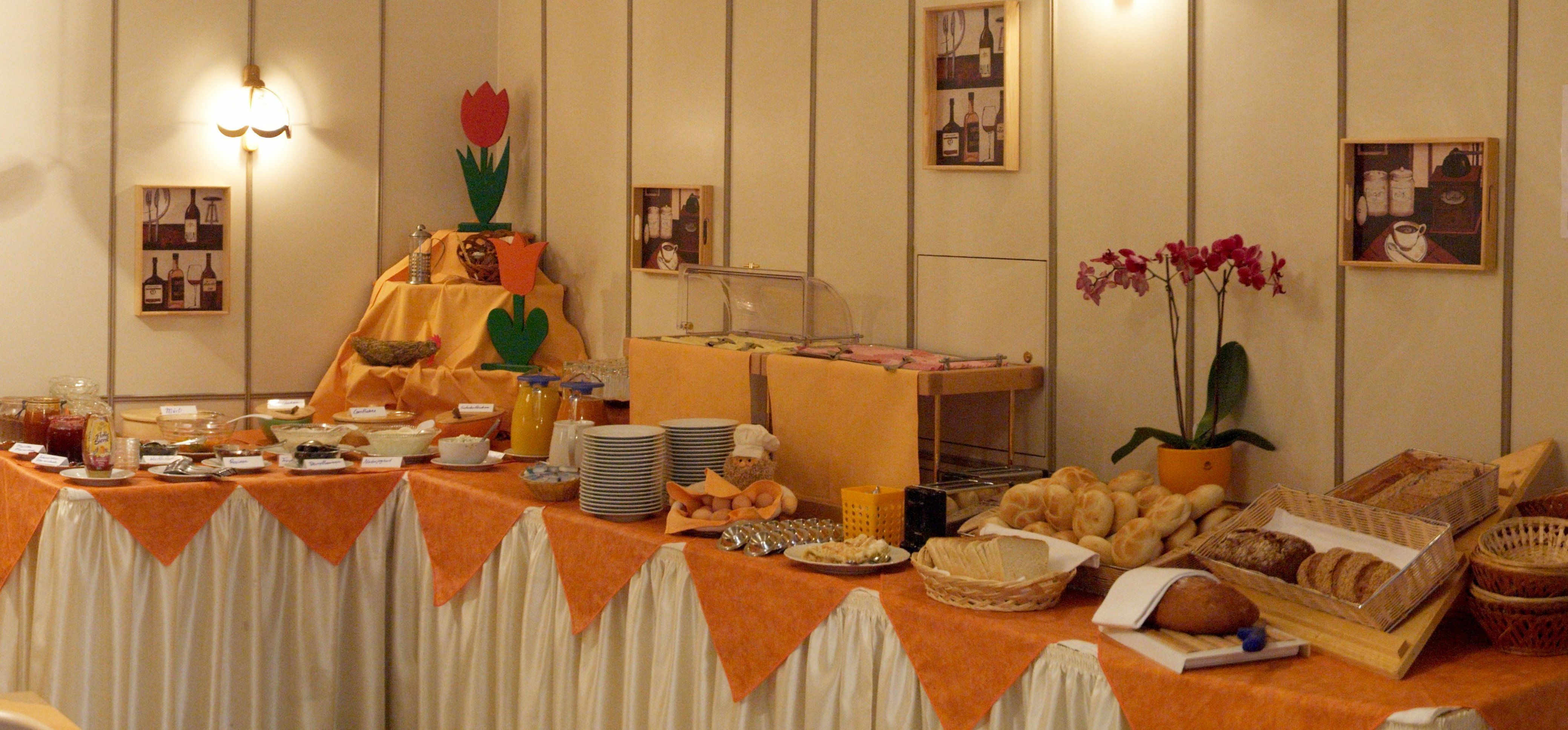 A rich breakfast buffet with bread, rolls, spreads and drinks on a table with an orange cloth.
