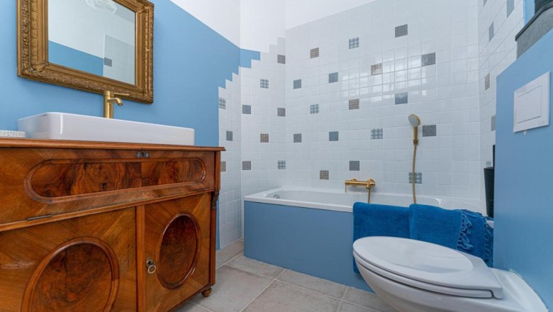 A bathroom with blue walls, a bathtub, a washbasin on a wooden cabinet and a golden mirror.