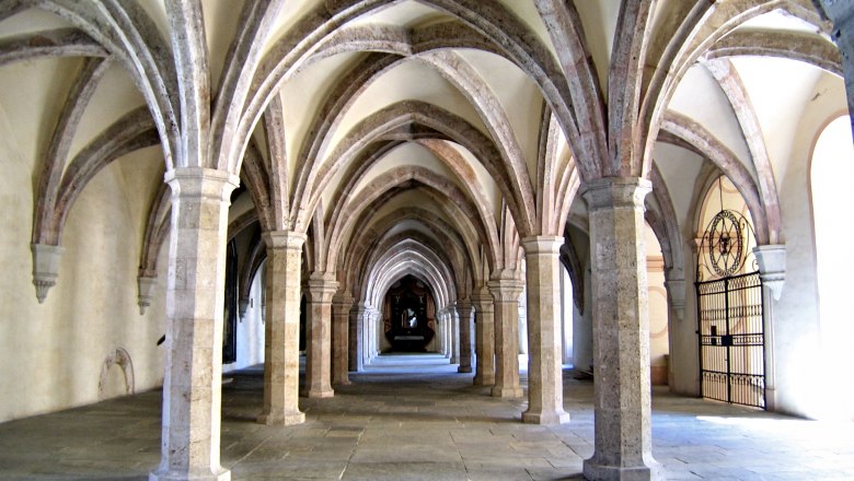 A medieval cloister with Gothic vaults and stone columns.