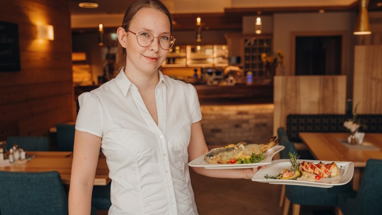 A woman in a restaurant carries two plates of food.
