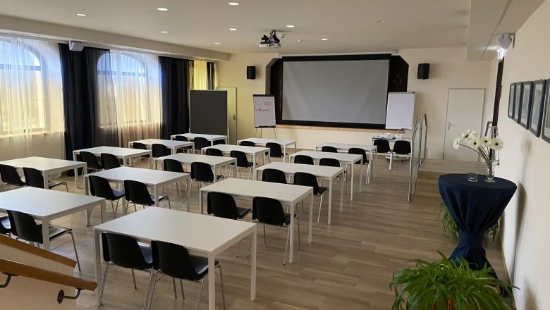 An empty seminar room with white tables, black chairs and a large screen at the front.