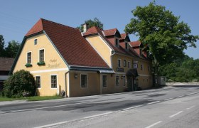 Yellow inn with a red roof on a road, surrounded by trees.