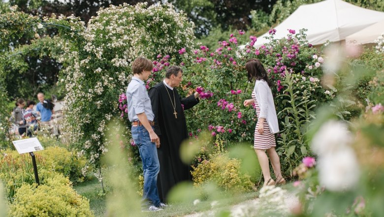 Three people are standing in a blooming garden and talking.