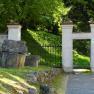 Stone gate with garden in the background, surrounded by trees.