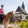 Two female riders on horses in front of a building with a tower.