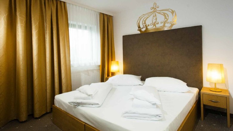 A double room with a large bed, golden curtains and two bedside tables with lamps.