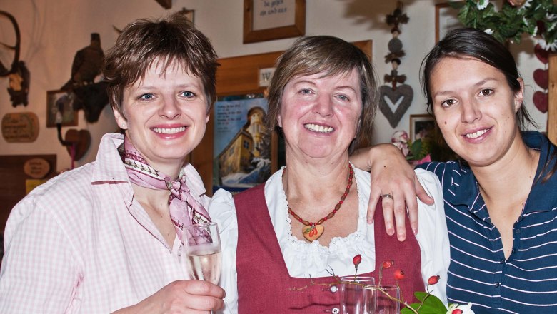 Three women smile at the camera and hold champagne glasses in their hands.