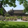 An old building in a garden with blooming roses and a bench in the foreground.