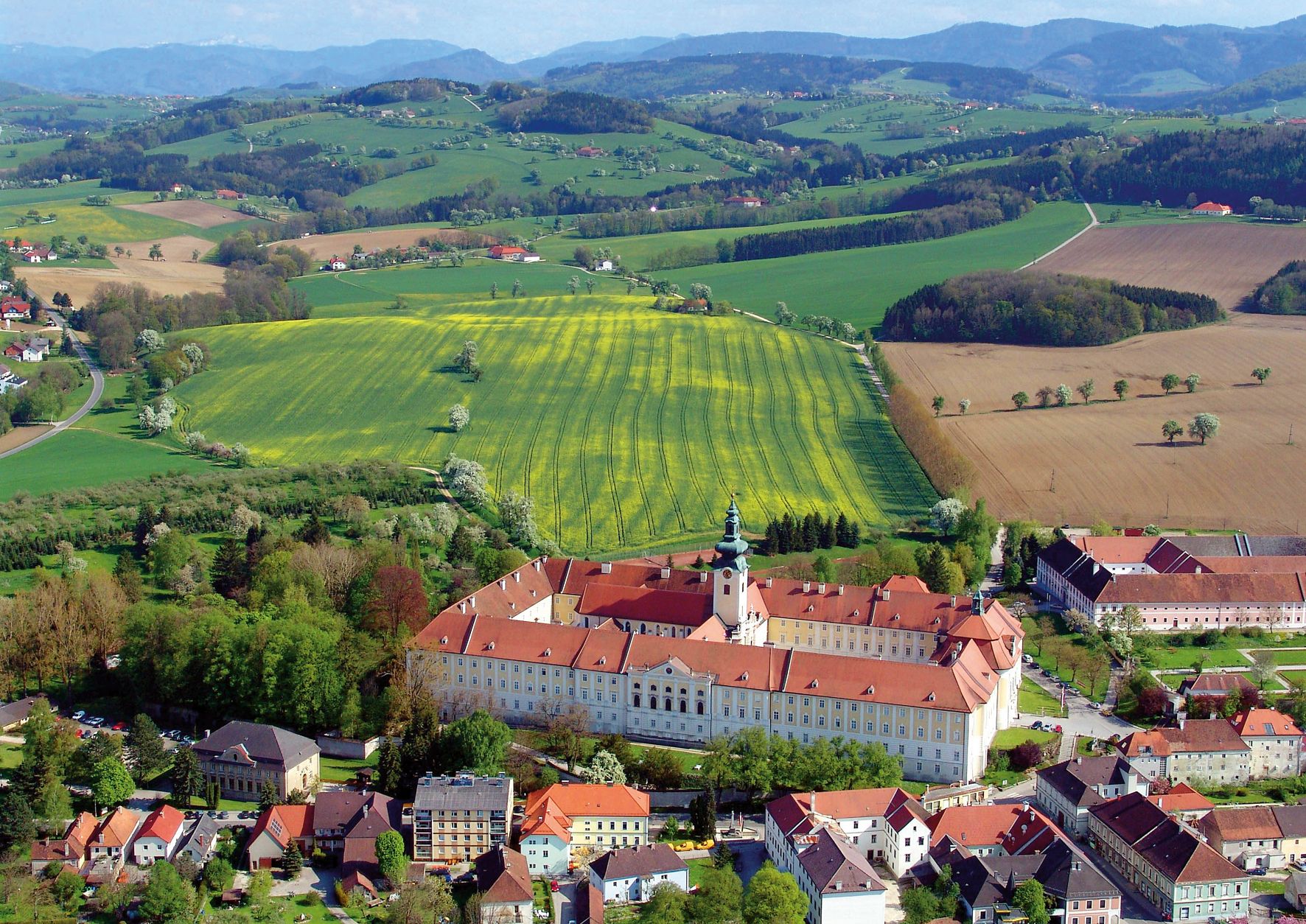 Aerial view of Seitenstetten Benedictine Abbey surrounded by green fields and hills.