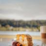 Piece of cake with strawberries and latte macchiato in front of a blurred landscape.