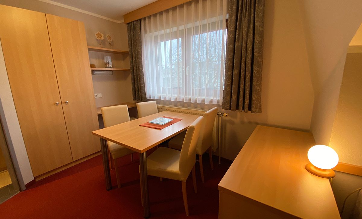A cozy room with wooden furniture, table, chairs and a window with curtains.
