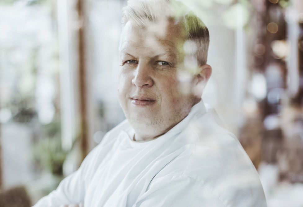 Portrait of a man in a white shirt, photographed through a window.
