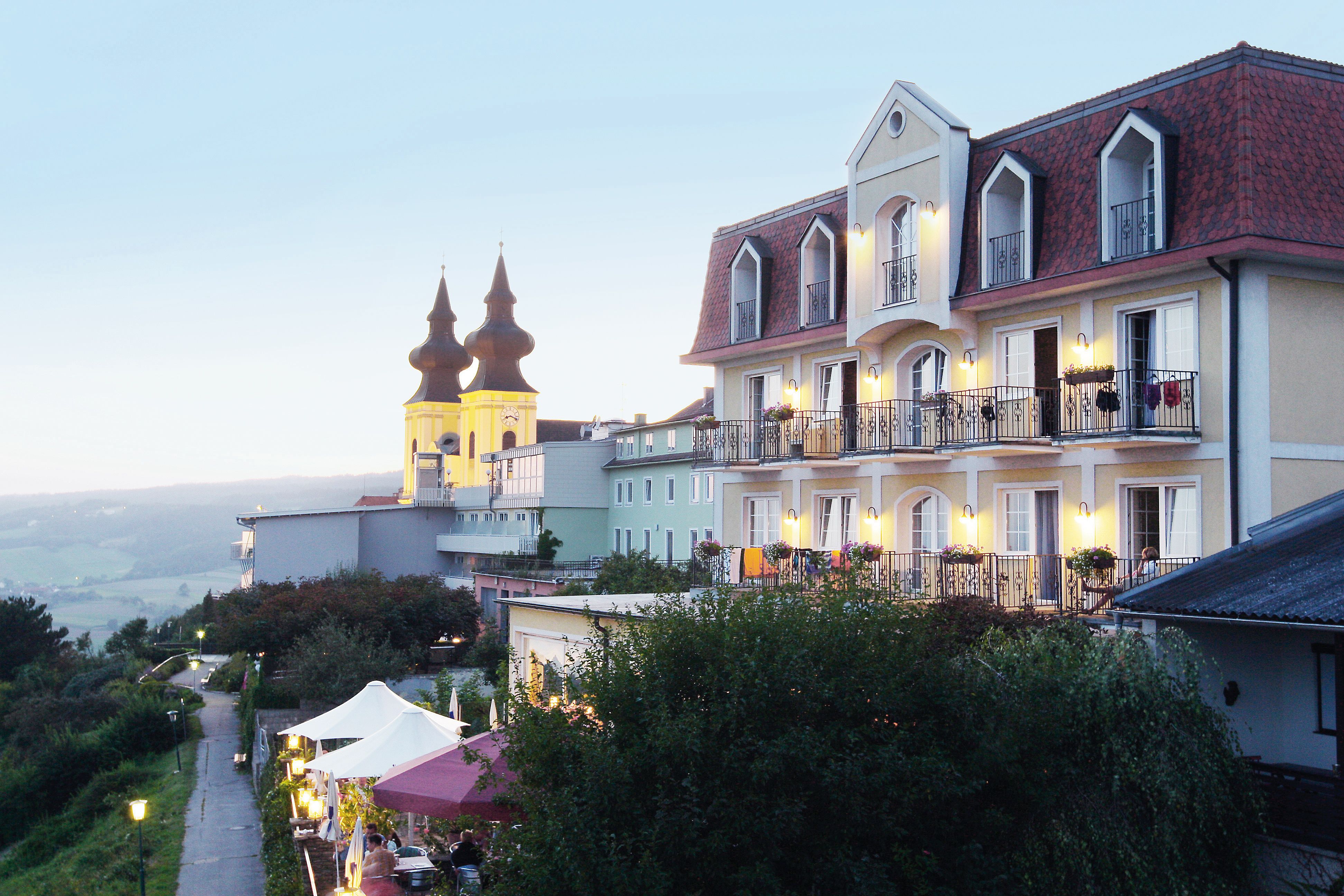 A hotel with balconies and a church in the background at dusk.